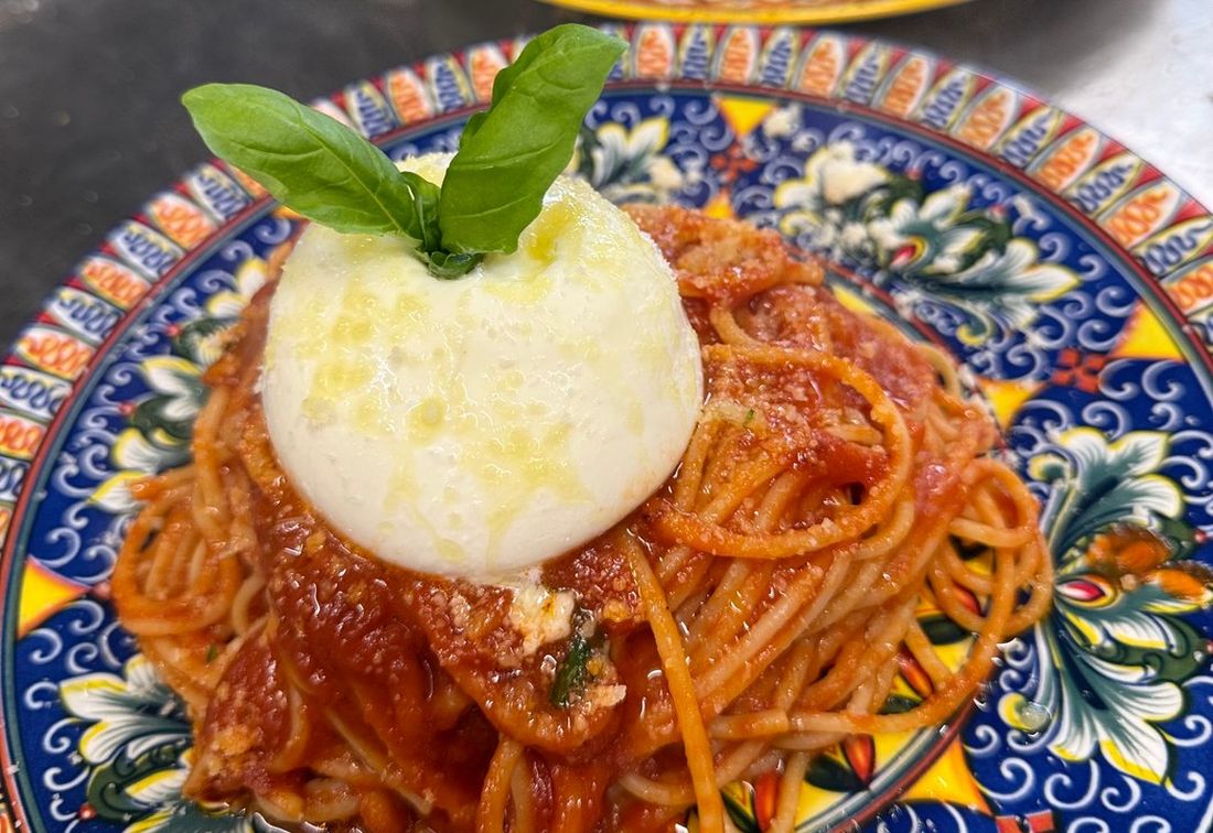 Spaghetti in Tomatensoße mit einer ganzen Burrata auf bunt bemaltem Keramikteller